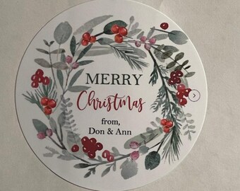 May include: A round white sticker with a watercolor wreath of green leaves and red berries. The text "Merry Christmas" is written in black cursive font. Below the wreath, the text "from, Don & Ann" is written in black font.