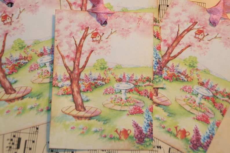 May include: Four vintage gift tags with a watercolor illustration of a pink flowering tree, a birdhouse, and a garden with flowers and a bird bath. The tags are tied with pink ribbon.