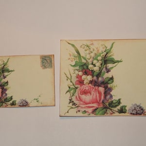 May include: Two vintage style blank cards with a floral design. The larger card features a bouquet of pink roses, white lilies of the valley, and purple flowers. The smaller card has a similar floral design with a pink rose and white lilies of the valley.