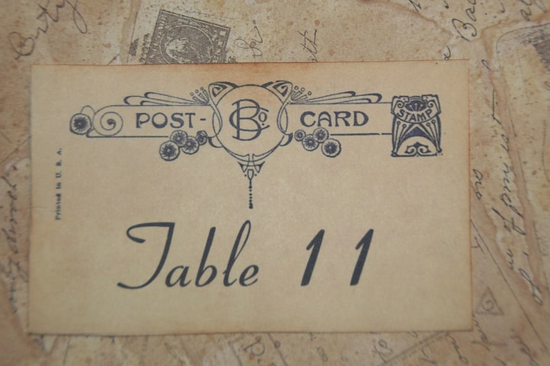 May include: Vintage-style table number card with the text "Table 11" in elegant script. The card features decorative elements and the words "POST-CARD" in a banner across the top. The background has a vintage paper texture.