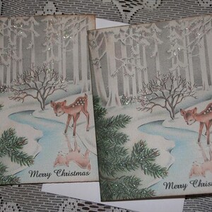 Peut inclure: Deux cartes de No&euml;l vintage repr&eacute;sentant une sc&egrave;ne de for&ecirc;t hivernale avec un faon pr&egrave;s d'un ruisseau. Les cartes pr&eacute;sentent un paysage enneig&eacute; avec des arbres et l'inscription "Merry Christmas". Les cartes sont d&eacute;cor&eacute;es de paillettes.