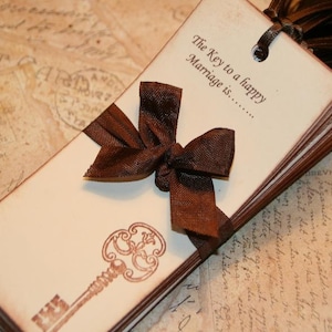 May include: A stack of cream-colored cards tied with a brown satin ribbon and a key-shaped design. The text on the cards reads "The Key to a happy Marriage is..."