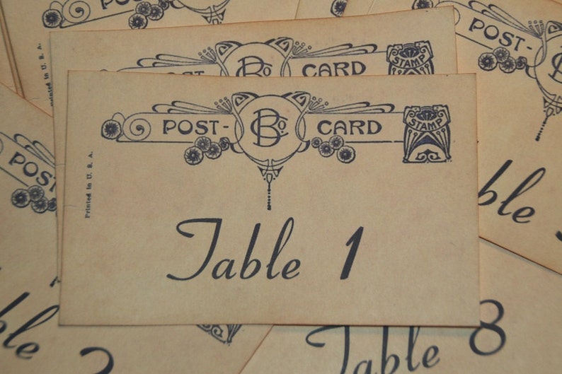 May include: Vintage postcard-style table cards with ornate blue designs and the text "POST-CARD" and "Table 1". The cards have a cream-colored background and are printed in the USA.