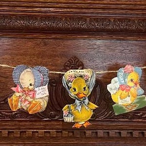 May include: A vintage Easter banner with a string of colorful paper cutouts featuring a bunny, chicks, and a cow. The banner is made of paper and has a rustic, vintage look.