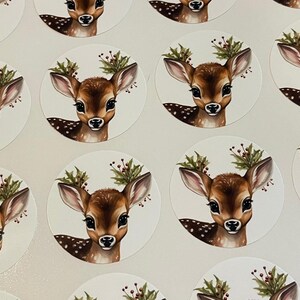 May include: A set of round stickers featuring a cute cartoon fawn with a red berry and green leaf wreath around its head. The fawn has brown fur with white spots and large brown eyes.