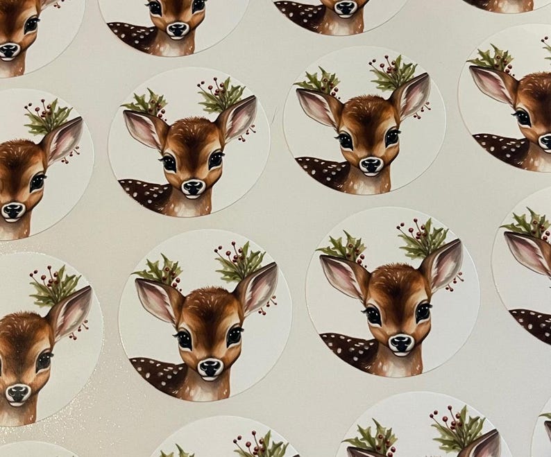 May include: A set of round stickers featuring a cute cartoon fawn with a red berry and green leaf wreath around its head. The fawn has brown fur with white spots and large brown eyes.
