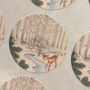 Peut inclure: Autocollants ronds repr&eacute;sentant une sc&egrave;ne de for&ecirc;t hivernale avec un faon. L'illustration montre un faon brun et blanc tachet&eacute; pr&egrave;s d'un ruisseau, entour&eacute; d'arbres enneig&eacute;s. L'arri&egrave;re-plan est une palette de couleurs douces et sourdes.