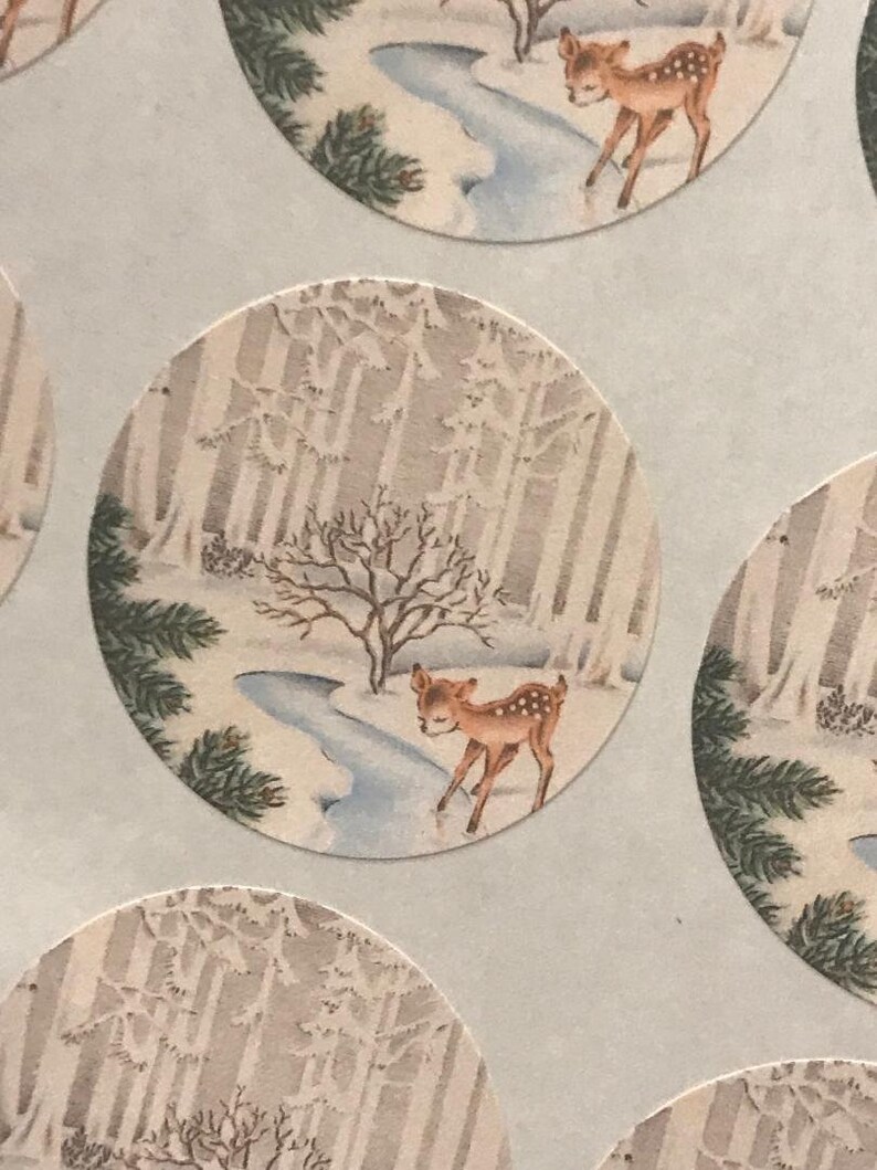 Peut inclure: Autocollants ronds repr&eacute;sentant une sc&egrave;ne de for&ecirc;t hivernale avec un faon. L'illustration montre un faon brun et blanc tachet&eacute; pr&egrave;s d'un ruisseau, entour&eacute; d'arbres enneig&eacute;s. L'arri&egrave;re-plan est une palette de couleurs douces et sourdes.