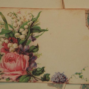 May include: A vintage postcard with a floral design featuring pink roses, white lilies of the valley, and purple flowers. The postcard has a blank space for writing a message and a vintage postage stamp in the upper right corner.