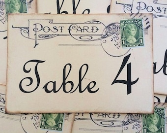 May include: Vintage-style table number card with the text "Table 4" printed in black script font on a cream background. The card is made to look like a vintage postcard with a stamp and postmark.