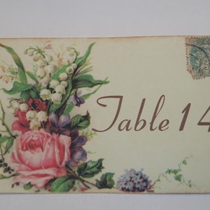 May include: A vintage-style table number card with a floral design. The card features a bouquet of pink roses, white lilies of the valley, and purple flowers. The text "Table 14" is printed in brown cursive font.