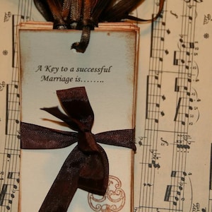 May include: A stack of blank cards tied with a brown ribbon and a bow. The cards have the text "A Key to a successful Marriage is..." printed on them. The cards are sitting on a sheet of music.