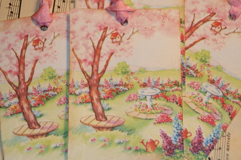 May include: Four vintage gift tags with a spring garden theme. Each tag features a pink flowering tree, a birdhouse, a small bird, and a bird bath. The tags are decorated with flowers and a watering can.