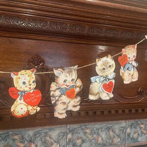 May include: A garland of vintage Valentine's Day cards featuring kittens with red hearts and messages like "For You" and "On Valentine's Day".