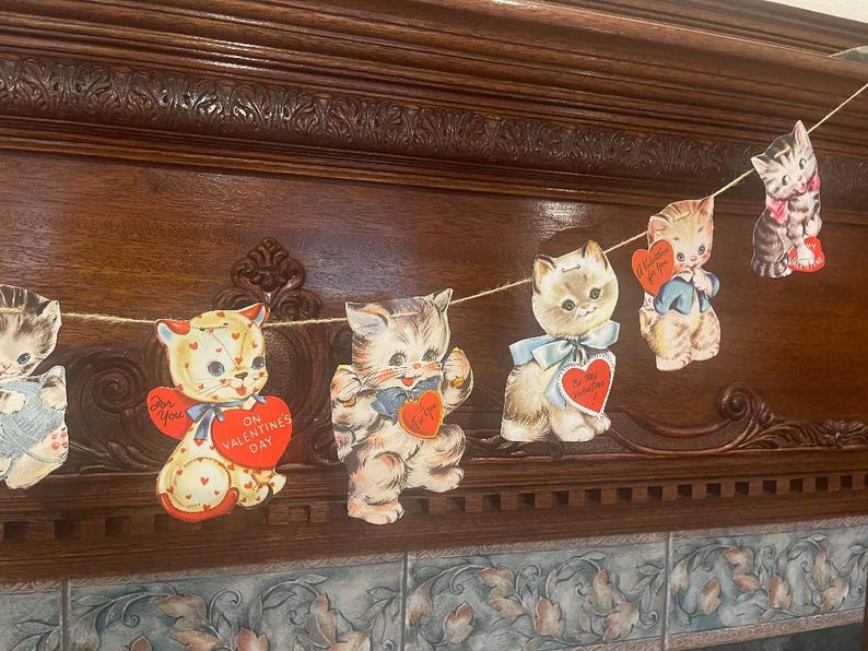 May include: A garland of vintage Valentine's Day cards featuring kittens with red hearts and messages like "For You" and "On Valentine's Day".