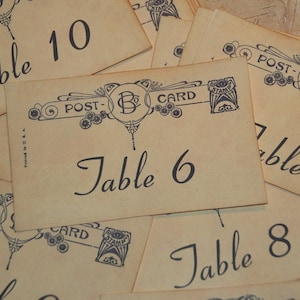 May include: Vintage-style table cards with numbers and the word "Table" in elegant script. Each card features a decorative border with the word "Postcard" and a stamp design. The cards are printed on aged paper.