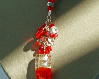 May include: A red beaded necklace with a silver chain and a red cord. The pendant features a cluster of red and clear beads, with a rectangular glass element at the bottom. The necklace is displayed against a gray background.