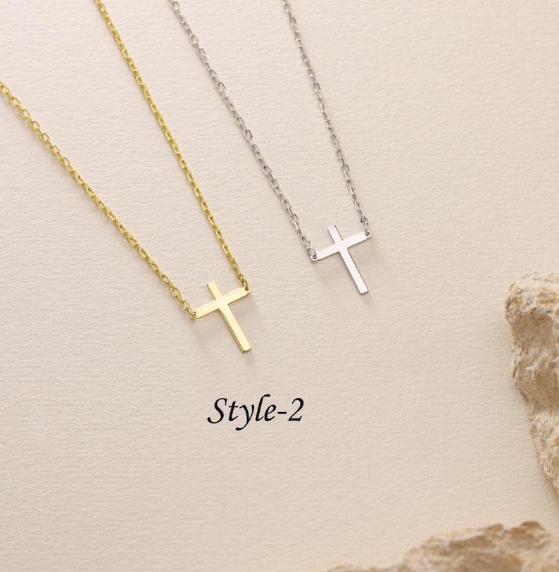 May include: Two delicate necklaces with a simple cross pendant. One necklace is gold and the other is silver. The necklaces are on a white background. Style-2