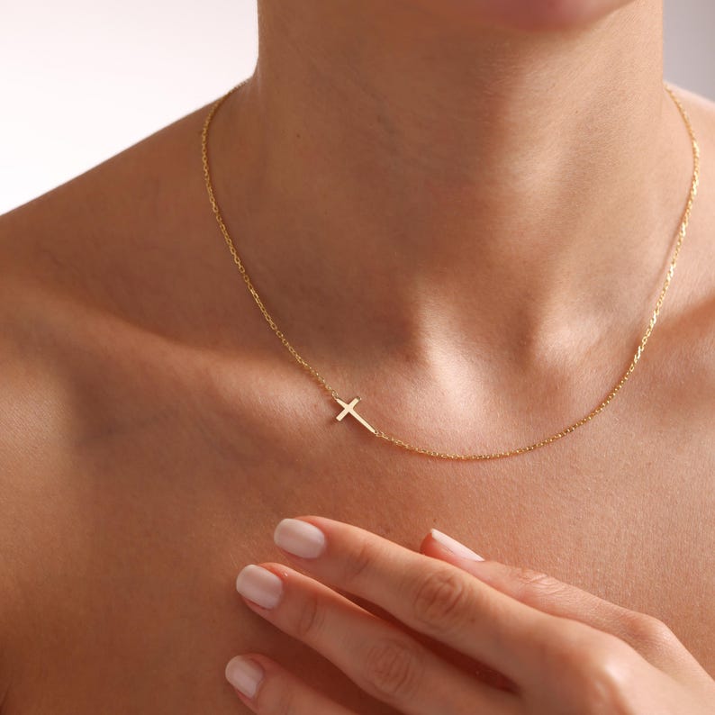 May include: A delicate gold chain necklace with a small, simple cross pendant.