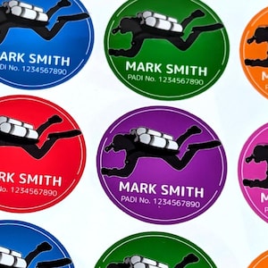Puede incluir: Un conjunto de diez pegatinas redondas con la silueta de un buceador en varios colores, incluyendo azul, verde, rojo, morado, naranja y rosa. Cada pegatina tiene el texto "MARK SMITH" y "PADI No. 1234567890".