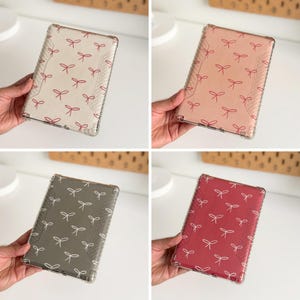 Peut inclure: Quatre étuis en plastique transparent pour liseuse, chacun avec un motif différent de nœuds roses sur fond blanc, rose, gris ou rouge.