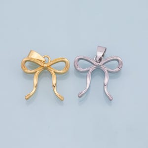 May include: Two bow-shaped pendants, one gold and one silver, are shown against a light blue background. The pendants are both about 2 inches long and have a simple, elegant design.