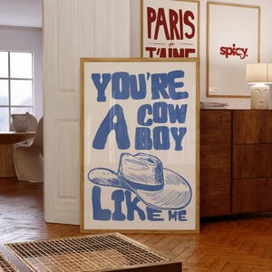 Puede incluir: Una impresi&oacute;n art&iacute;stica enmarcada con el texto "YOU'RE A COWBOY LIKE ME" en azul, con una ilustraci&oacute;n de sombrero de vaquero. Se ven otras dos impresiones enmarcadas, una con "PARIS je t'aime" y otra con la palabra "spicy."
