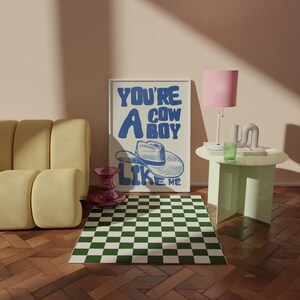 Puede incluir: Escena de una habitaci&oacute;n con un p&oacute;ster enmarcado con el texto "YOU'RE A COWBOY LIKE ME" y una ilustraci&oacute;n de sombrero de vaquero. La habitaci&oacute;n incluye un sof&aacute; amarillo, una alfombra a cuadros verdes y blancos y una l&aacute;mpara rosa.