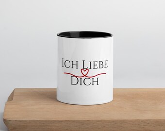 Può includere: Tazza in ceramica bianca con bordo e manico neri. La tazza ha il testo "ICH LIEBE DICH" in nero con un cuore rosso al centro del testo.