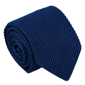 Può includere: Una cravatta blu navy profondo con una distinta trama lavorata a maglia. La cravatta è arrotolata in una spirale compatta, mostrando il motivo intrecciato coerente e su piccola scala sull'intera superficie del tessuto, terminando con una punta quadrata.