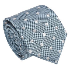 Op de afbeelding: Opgerolde blauwe stropdas met een klein wit bloemenpatroon. De stropdas heeft een geruite achtergrond en is gemaakt van een gladde stof. Een klassiek accessoire voor formele of zakelijke kleding.