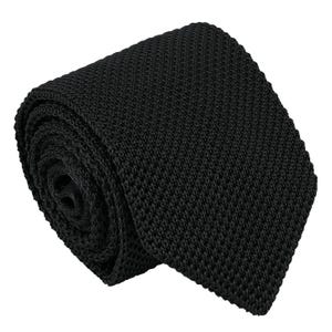 May include: A solid black necktie featuring a distinct knit texture. The tie is rolled into a circular shape, showcasing the consistent woven pattern of the fabric throughout the entire length of the accessory. The material has a matte finish.