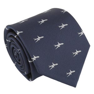 Può includere: Una cravatta blu navy scuro con un motivo ripetuto di piccoli aerei bianchi ricamati. Il tessuto ha una trama visibile e la cravatta è arrotolata a spirale, mostrando l'estremità appuntita e gli strati ripiegati del materiale.
