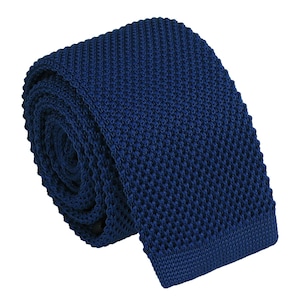 Könnte beinhalten: Eine einfarbige marineblaue Krawatte mit einer ausgeprägten, strukturierten Strickoptik. Die Krawatte ist kreisförmig aufgerollt und zeigt das gleichmäßige Webmuster sowie das flache, quadratische Ende. Die tiefblaue Farbe ist durchgehend einheitlich und unterstreicht die komplexe, kleinteilige gitterartige Struktur des gestrickten Stoffes.