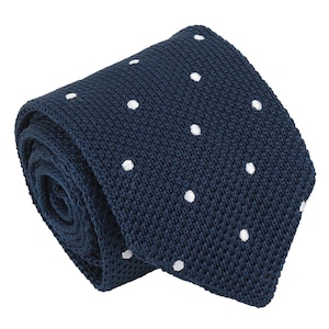 Puede incluir: Una corbata de punto en color azul marino oscuro con un patrón repetitivo de pequeños lunares blancos. La corbata presenta una apariencia tejida y texturizada con un extremo cuadrado, mostrando una estructura de tejido consistente en todo.