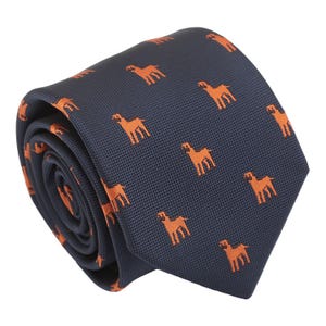 Op de afbeelding: Een donkerblauwe zijden stropdas met een herhalend patroon van oranje honden. De stropdas is opgerold en klaar om te dragen.