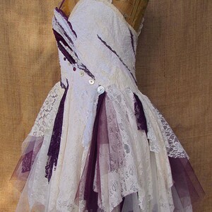 May include: A white and purple layered lace dress with a ruffled skirt and a fitted bodice. The dress is decorated with buttons and has a vintage aesthetic.