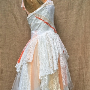 May include: A white lace dress with a peach tulle overlay and a peach ribbon detail. The dress is on a dress form and has a layered skirt.