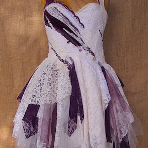 May include: A white and purple lace dress with a layered skirt and a fitted bodice. The dress is decorated with buttons and has a vintage aesthetic.