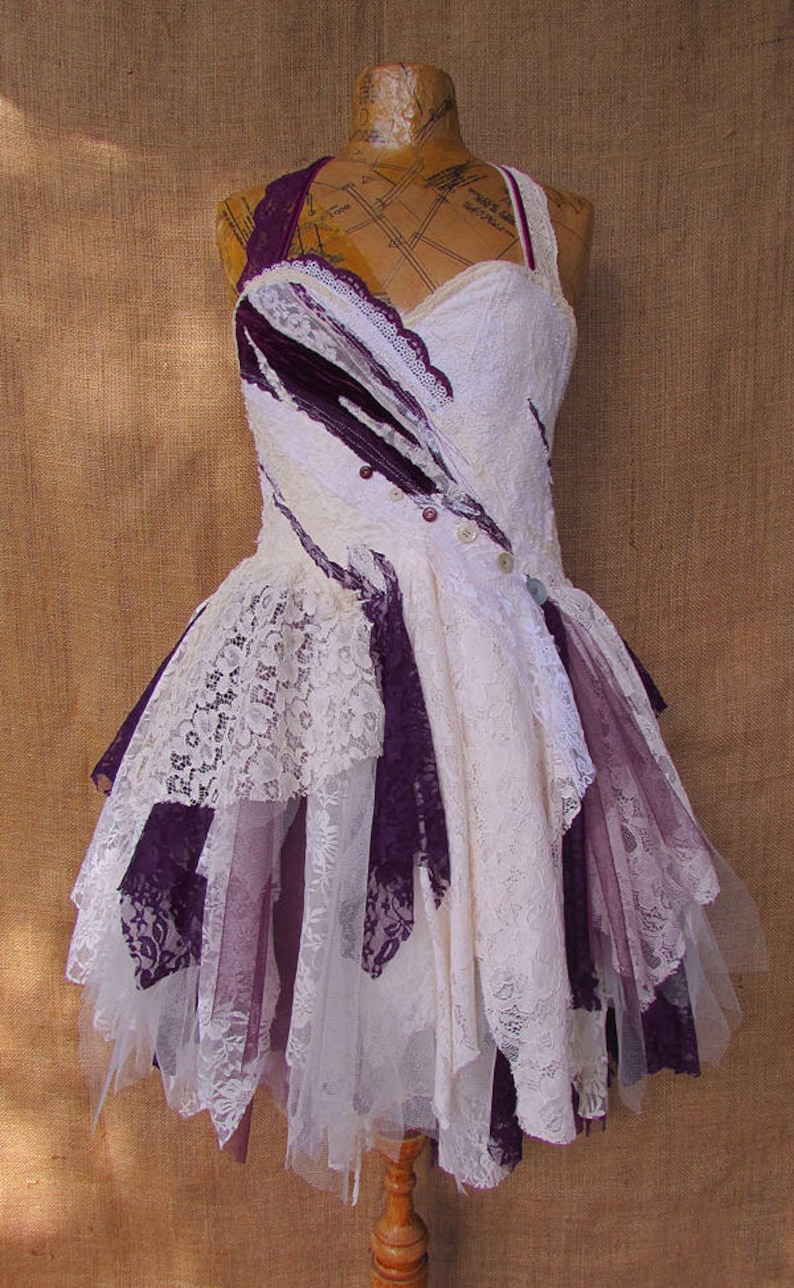 May include: A white and purple lace dress with a layered skirt and a fitted bodice. The dress is decorated with buttons and has a vintage aesthetic.