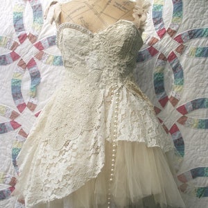 May include: A white lace dress with a tulle underskirt and a pearl necklace. The dress is on a mannequin and has a vintage style.