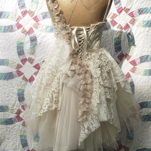 Puede incluir: Un vestido de novia de encaje blanco con una falda de tul y un corpi&ntilde;o de encaje. El vestido tiene una espalda de cors&eacute; con un lazo de cinta de sat&eacute;n. El vestido est&aacute; decorado con delicadas flores de encaje.