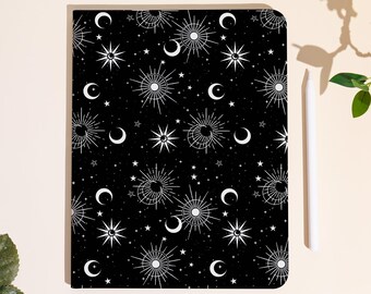 May include: Black notebook with a celestial pattern of white stars, moons, and sunbursts. A white stylus rests on the side. The notebook's design features a repeating pattern of celestial bodies.