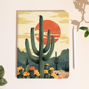 May include: A notebook featuring a desert landscape illustration. The cover displays a large green saguaro cactus with a setting sun in the background. Yellow and orange flowers bloom at the base of the cactus. A white stylus rests beside the notebook.