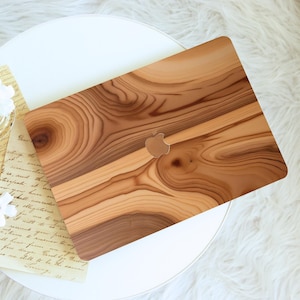May include: A wooden-textured laptop case with a natural wood grain pattern. The case has a cutout for the Apple logo and is displayed on a white surface. The case is a warm brown color.