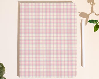 Può includere: Un quaderno rettangolare con un motivo a quadri rosa, azzurro e crema. Uno stilo bianco è appoggiato sul lato destro del quaderno. Il quaderno è su una superficie color crema.