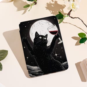 May include: A black cat illustration on a black background, holding a glass of red wine with the moon in the background. The cat is in a celebratory pose, with its arms raised. The design is on a black rectangular product.