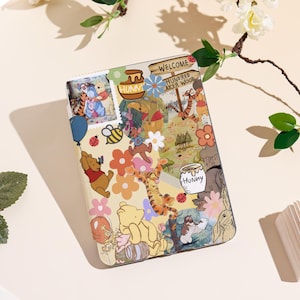 May include: A decorative case with a collage of Winnie the Pooh characters and imagery. The design includes illustrations of Pooh, Piglet, Tigger, and Eeyore, along with flowers, bees, and the text "Welcome Hundred Acre Wood" on a sign.
