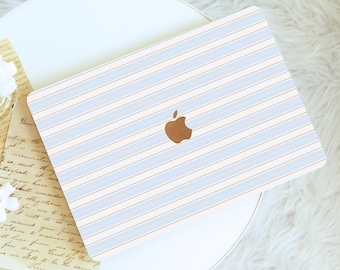 Może przedstawiać: Laptop z jasnoniebiesko-białym wzorem w paski. Laptop ma brązowe logo Apple pośrodku. Laptop leży na białym stole z białym, puszystym dywanem w tle.