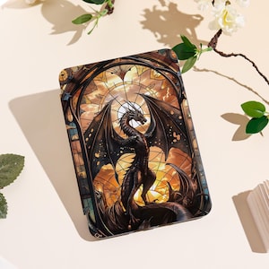 May include: A phone case featuring a stained-glass design with a dragon. The dragon is black and red, with large wings, set against a sunset background. The case has a protective design.